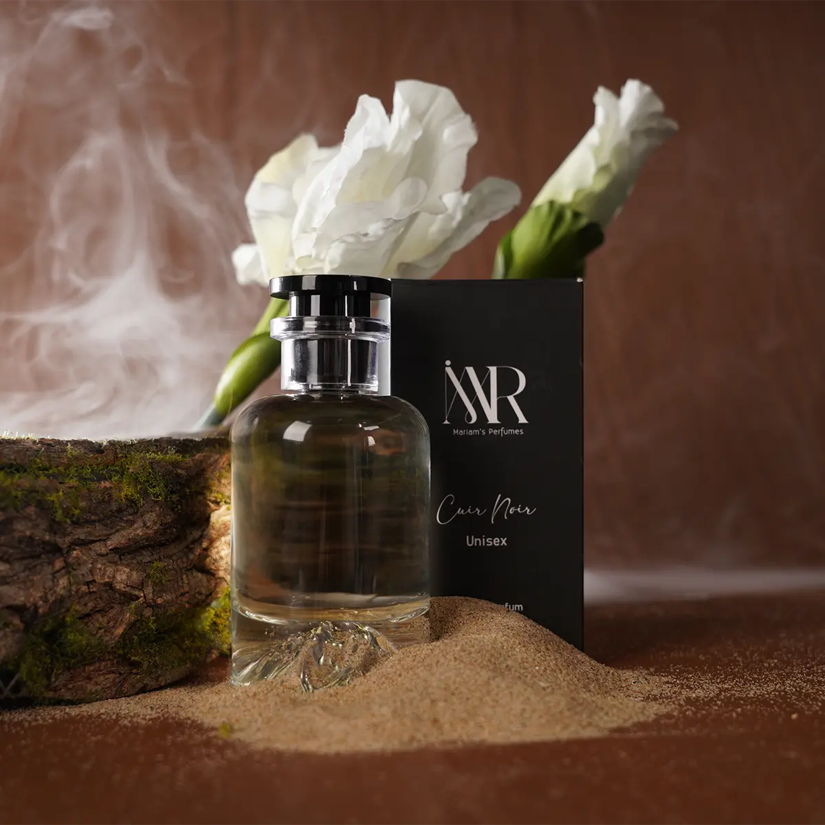 Cuir Noir bottle resting in sand beside its black box, with white flowers and smoke